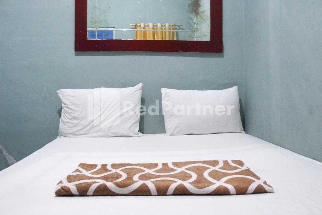 een bed met witte lakens en kussens in een kamer bij Snow White Residence near Grogol Mitra RedDoorz in Jakarta