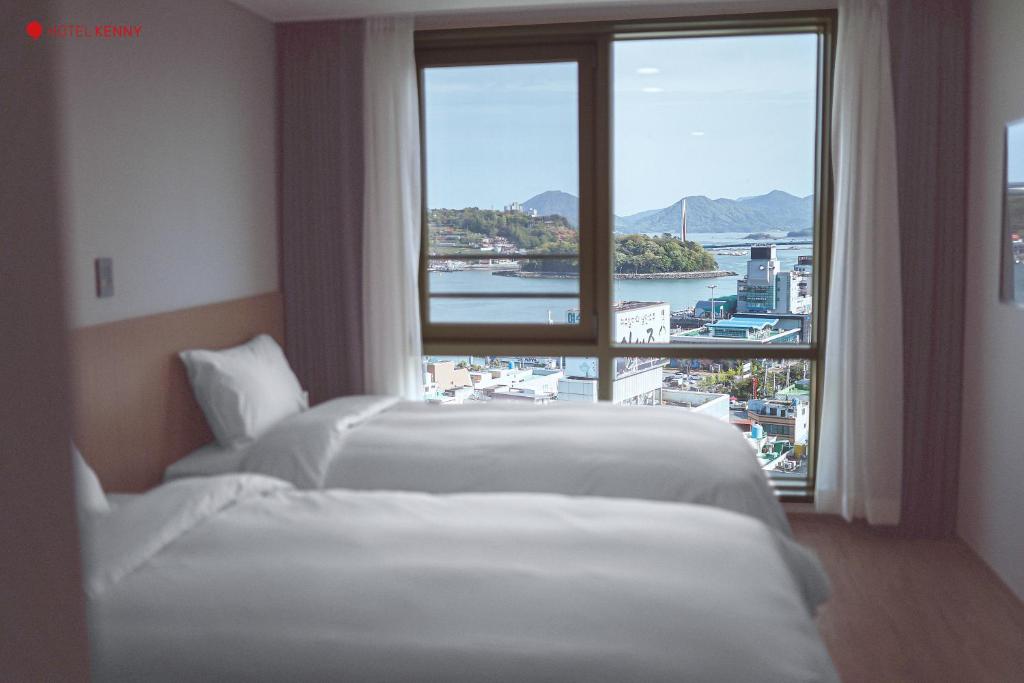two beds in a hotel room with a large window at Hotel Kenny Yeosu in Yeosu