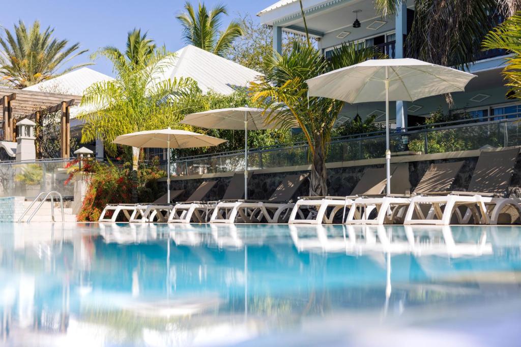 a pool with chairs and umbrellas in front of a building at Hôtel Les Créoles in Saint-Gilles les Bains