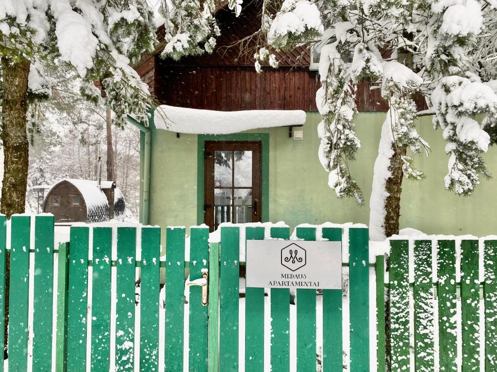 a green fence with a sign in front of a house at Medaus apartamentai in Trakai
