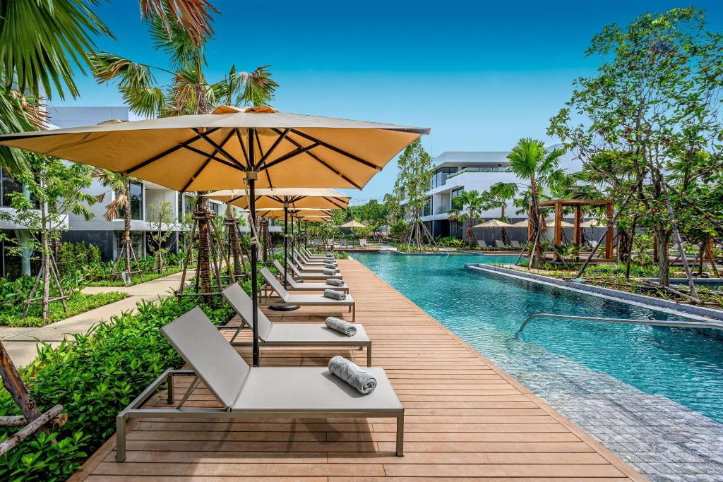 a row of lounge chairs with umbrellas next to a swimming pool at Stay Wellbeing & Lifestyle Resort in Rawai Beach