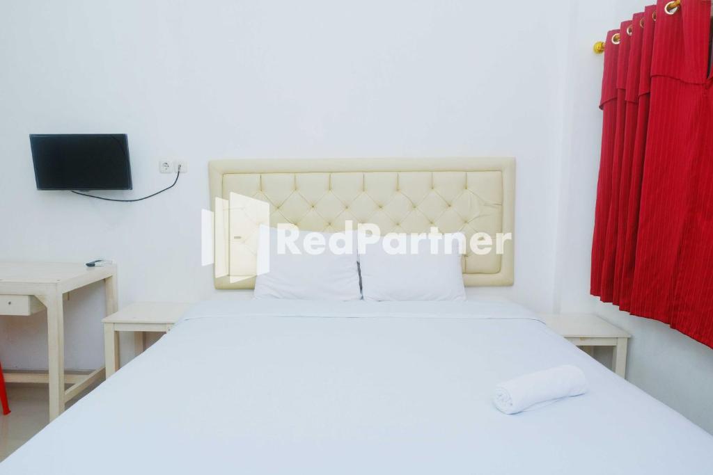 Fortuner Homestay Syariah Makassar Mitra RedDoorz في Pampang: غرفة نوم بسرير ابيض وستارة حمراء