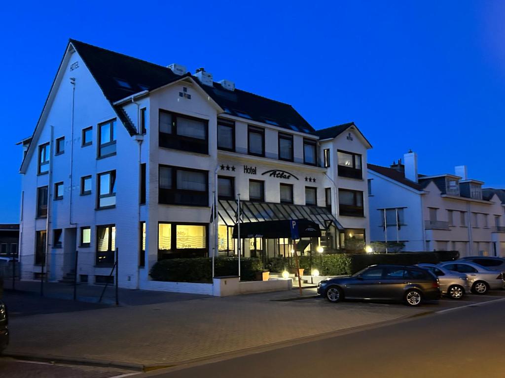 un grand bâtiment blanc avec des voitures garées dans un parking dans l'établissement Hotel Atlas, à Zeebruges