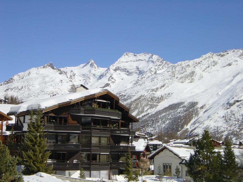 a large building with snow covered mountains in the background at Haus Allegra Panorama in Saas-Fee