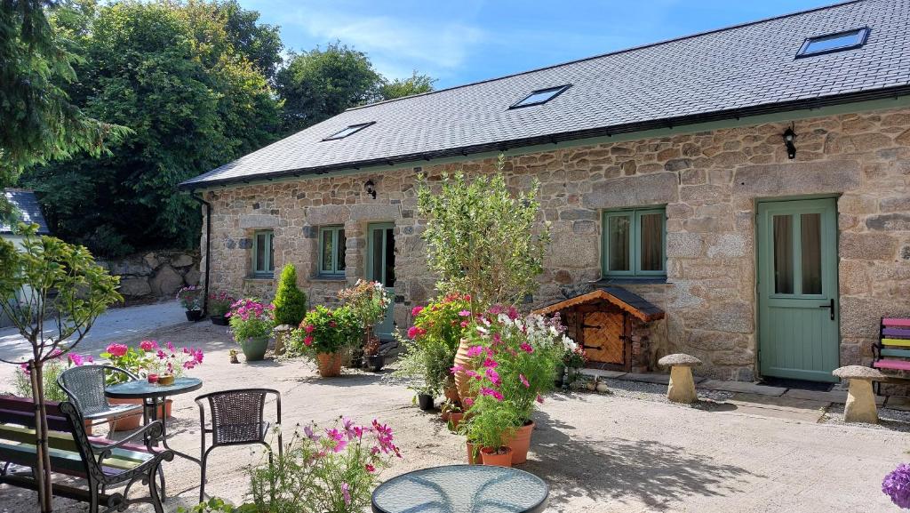 une maison en pierre avec une table, des chaises et des fleurs dans l'établissement Wesley House Holidays - Choice of 2 Quirky Cottages in 4 private acres, à Redruth