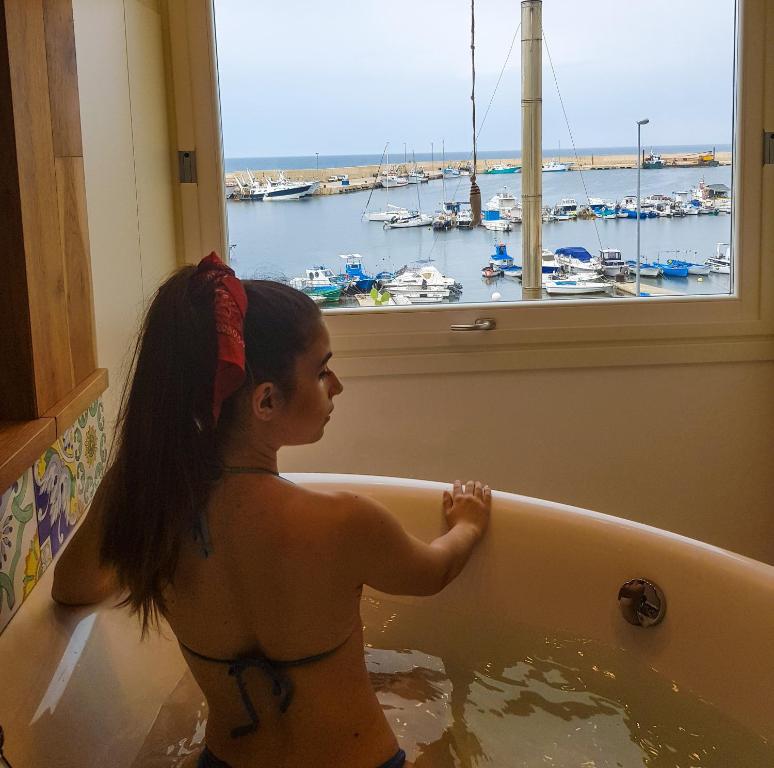 a young girl sitting in a bath tub looking out a window at B&B 106 Maison de Charme in Mola di Bari