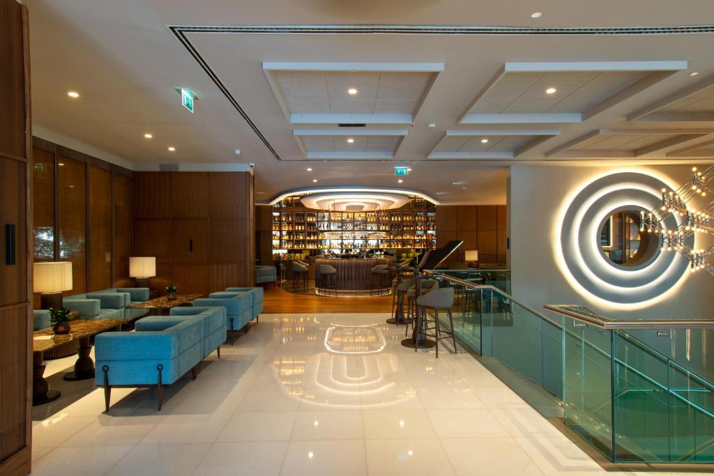 A polished lobby lounge with blue seating, a glass-railed stair and a backlit bar.