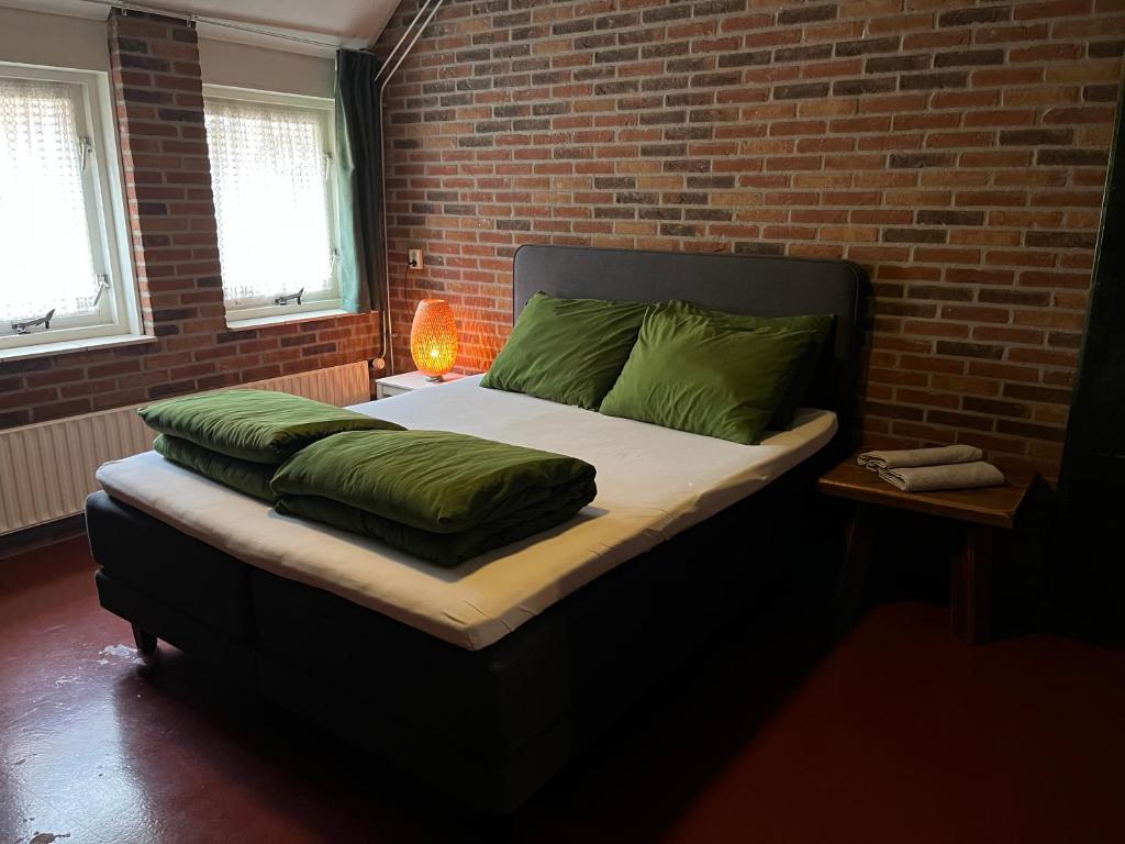 een slaapkamer met een bed met groene kussens en een bakstenen muur bij Familiehuis voor 13 personen in Diever