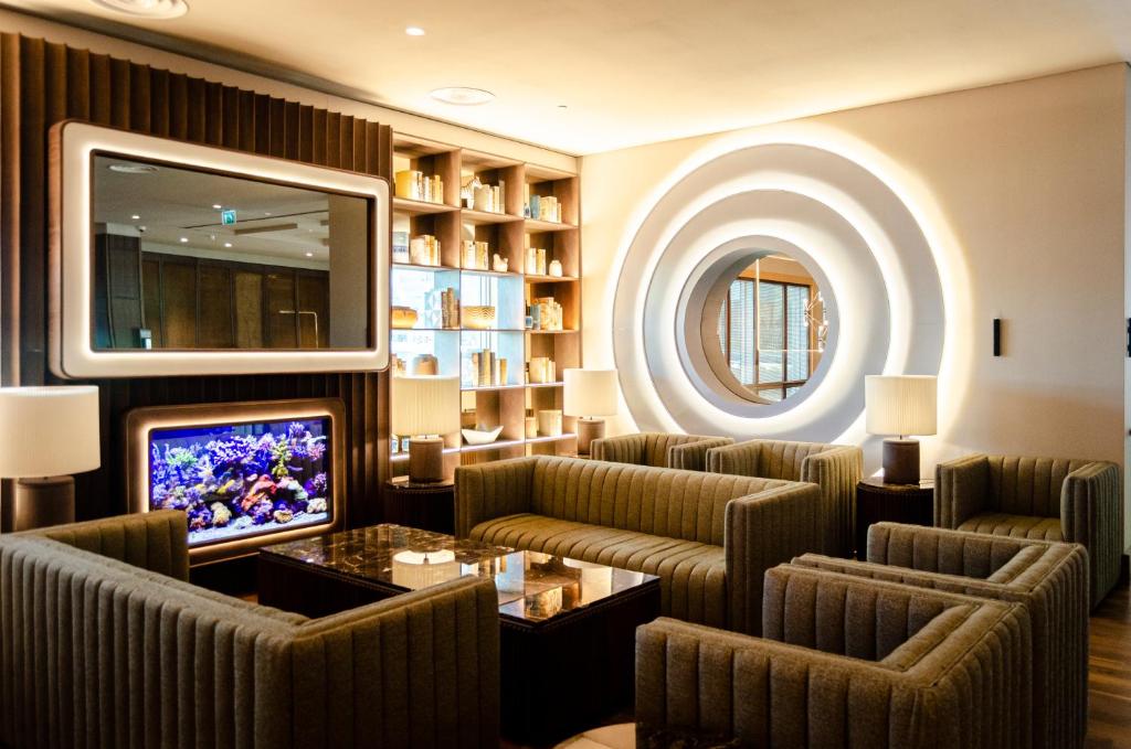 A warmly lit hotel lounge with deep upholstered seating, a television and a circular wall mirror.