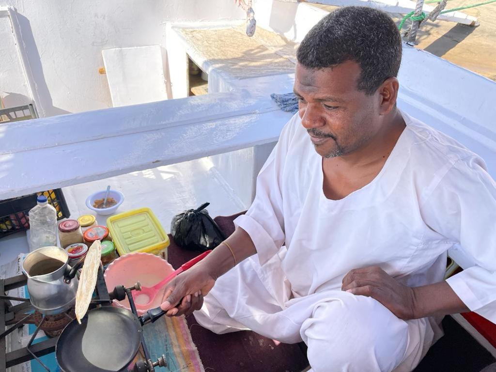 un hombre sentado en una mesa agitando una olla en My Dream Nile Felucca en Asuán