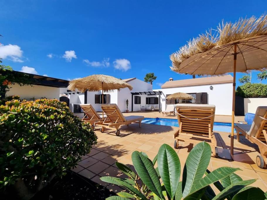 um pátio com cadeiras e guarda-sóis e uma piscina em Surf&fun heated pool villa em La Oliva