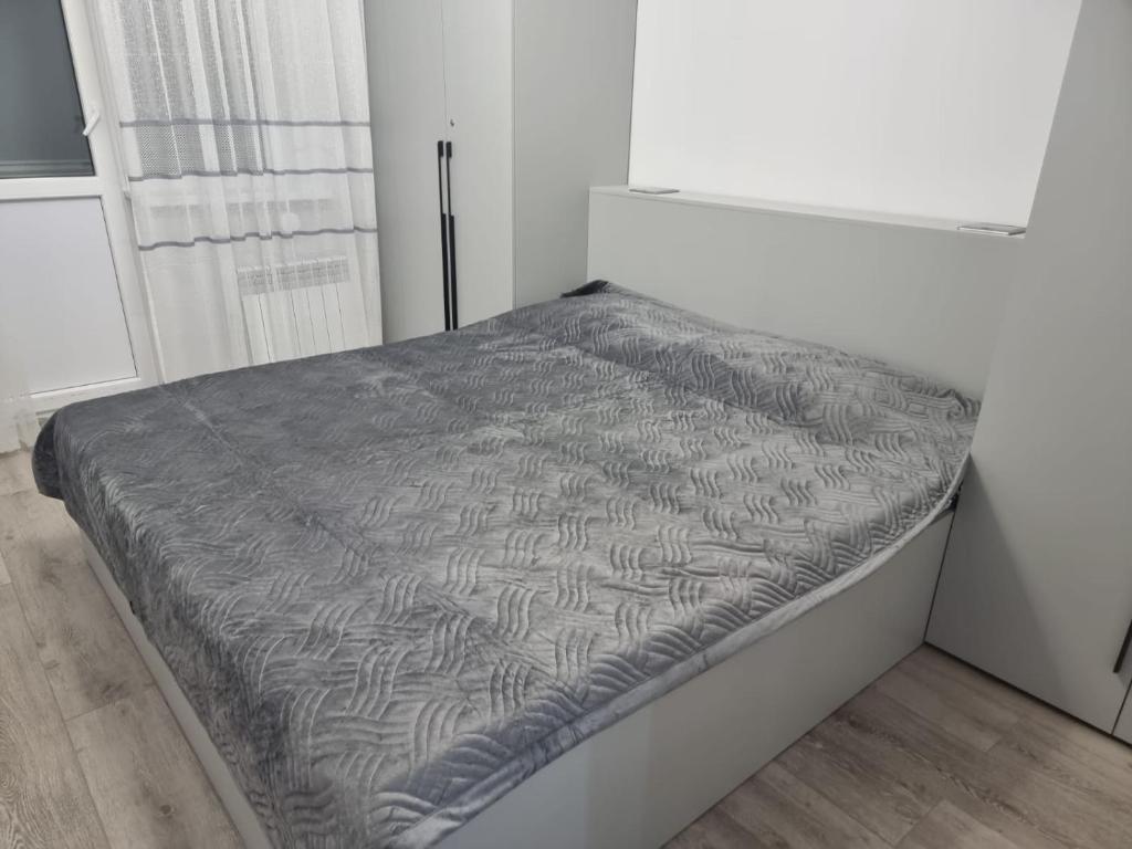 een bed in een witte kamer met een grijs dekbed bij Однокомнатная квартира in Taldykolʼ