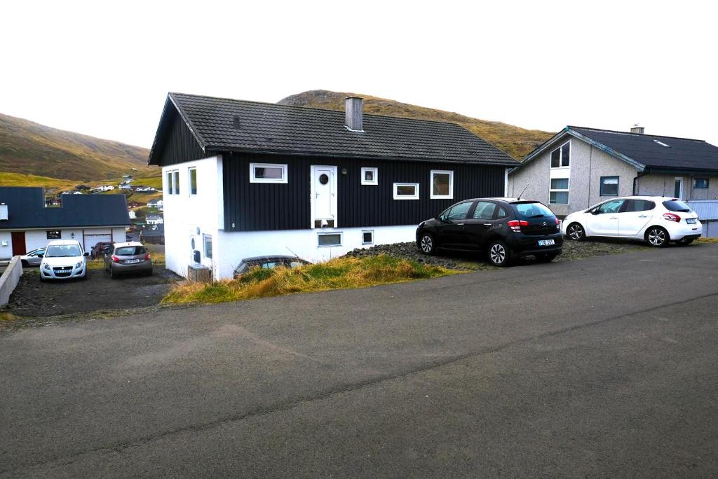 a black and white house with cars parked in a parking lot at Pouls Airport Guesthouse - PHD Car Rent in Sørvágur
