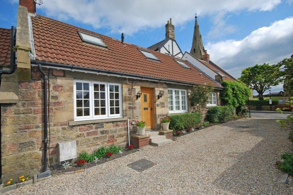 an old brick house with a yellow door and a church at Grange Cottage in Alnmouth