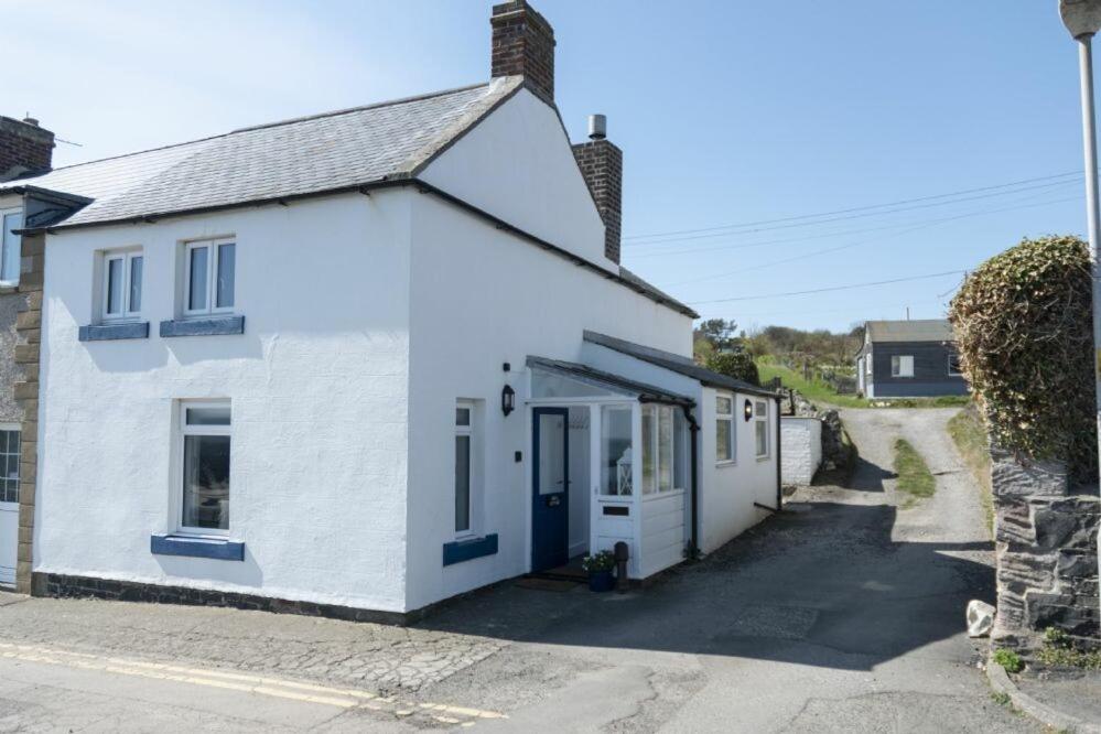 a white cottage with a blue door on a street at Creel Cottage, Craster in Craster