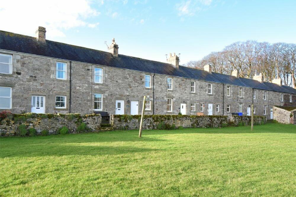 a large brick building with a grass field in front of it at Farne View Cottage in Seahouses