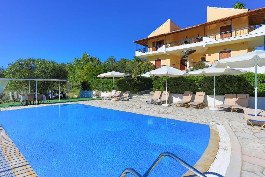 una piscina con sillas y sombrillas junto a un edificio en Cochelli Upper Pool Walk to beach AC WiFi, en Ágios Stéfanos