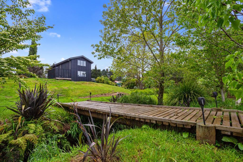 a wooden bridge in a garden with a black building at The Barn - Waihi Holiday Home in Waihi