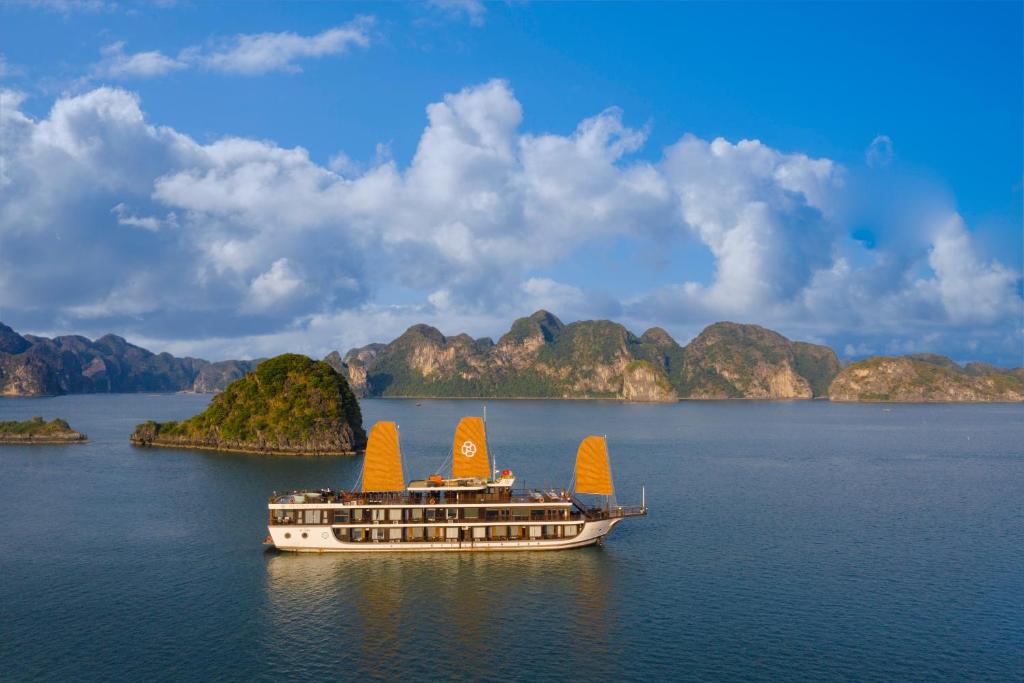 un bateau sur l'eau avec des montagnes en arrière-plan dans l'établissement Peony Cruises, à Hạ Long