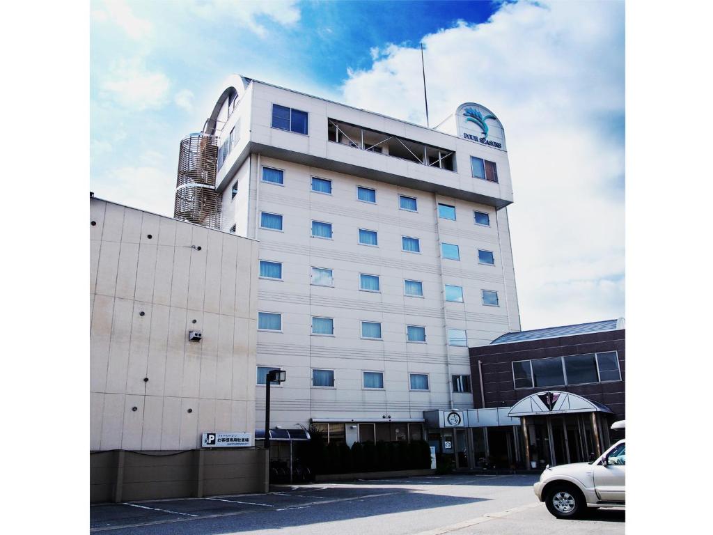 Takayama City Hotel Four Seasons في تاكاياما: مبنى أبيض طويل وبه سيارة متوقفة أمامه