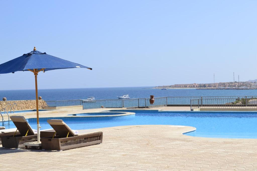 a swimming pool with chairs and an umbrella and the ocean at La Siesta Hotel Al Sokhna in Ain Sokhna