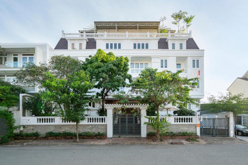 a white building with a gate and trees in front at M Village Nguyễn Văn Hưởng in Ho Chi Minh City