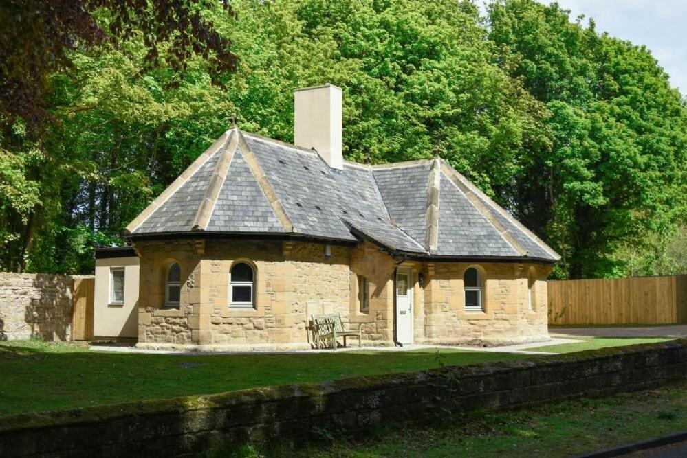 a small stone house with a roof on a field at The Lodge Alnwick in Alnwick