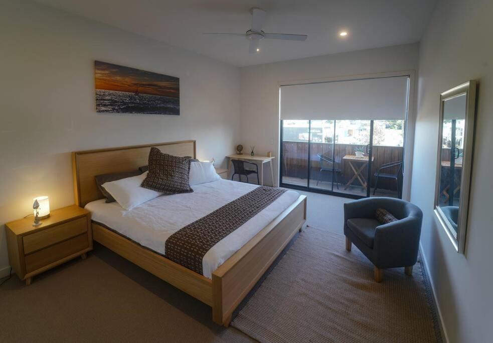 a bedroom with a bed and a chair and a window at Modern air-conditioned 3-bedroom townhouse in centre of Cape Woolamai in Cape Woolamai