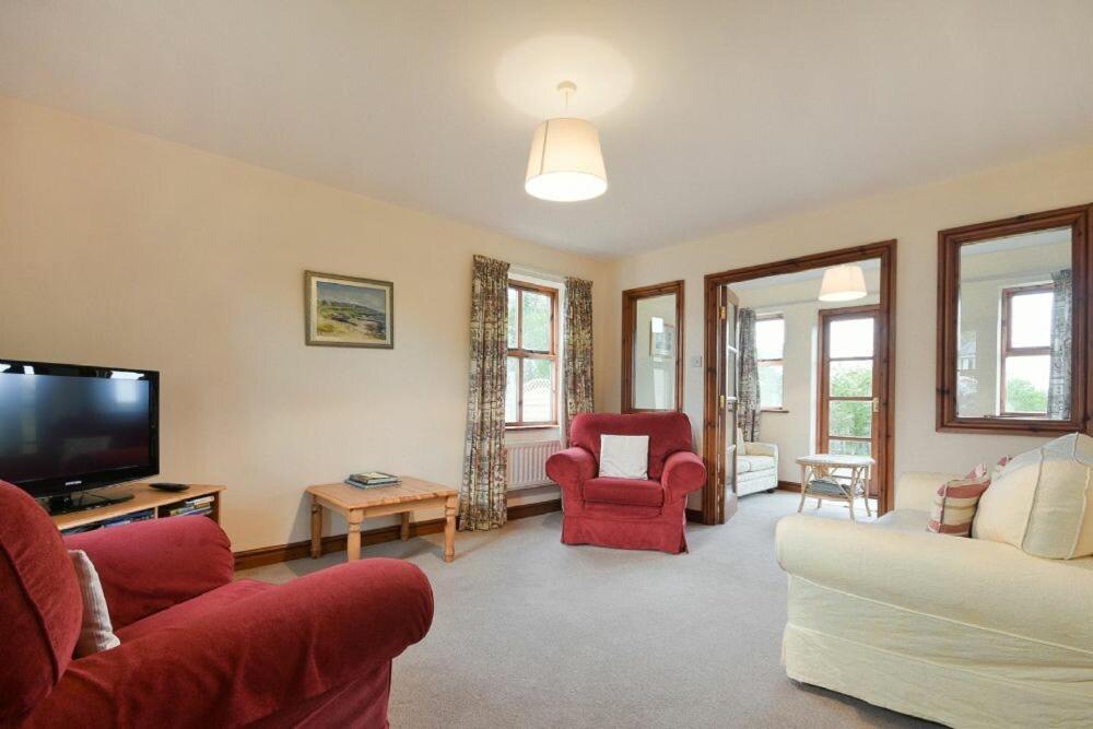 sala de estar con sillas rojas y TV de pantalla plana en Smithy Court, en Craster
