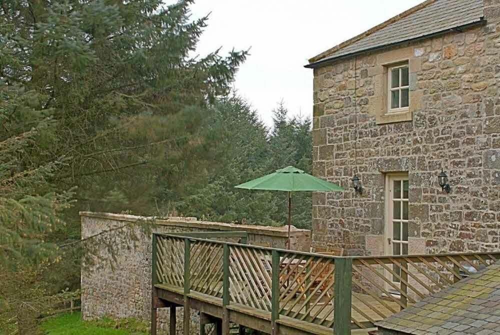 a green umbrella sitting on a deck next to a building at The Bolthole in Eglingham