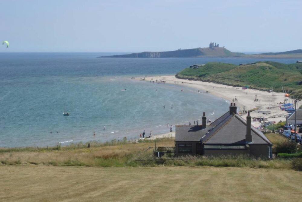 a beach with people in the water and a building at Melvin Cottage in Embleton
