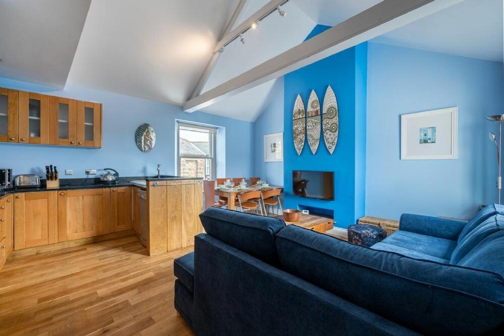 a blue living room with a couch and a kitchen at Pilots Rest in Alnmouth