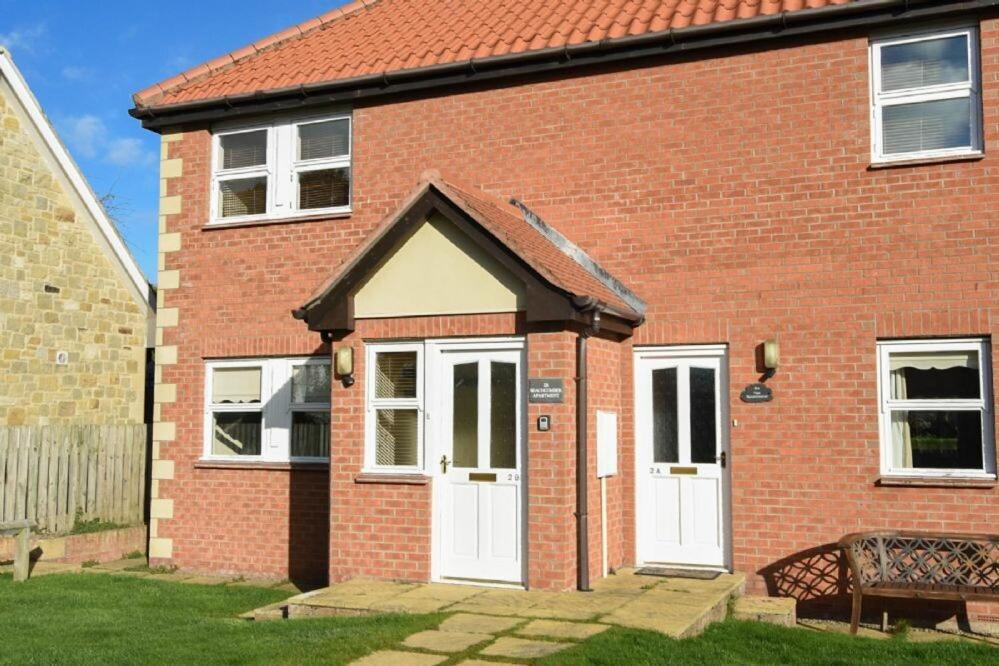 a brick house with white doors and a bench at Beachcomber Apartment in Bamburgh