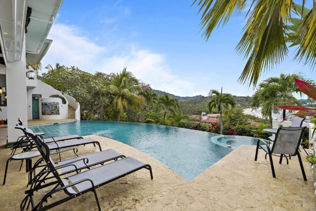 una piscina resort con sillas y vistas al océano en Ocean-View Flamingo Palace with Stone Courtyard and Giant Infinity Pool, en Playa Flamingo