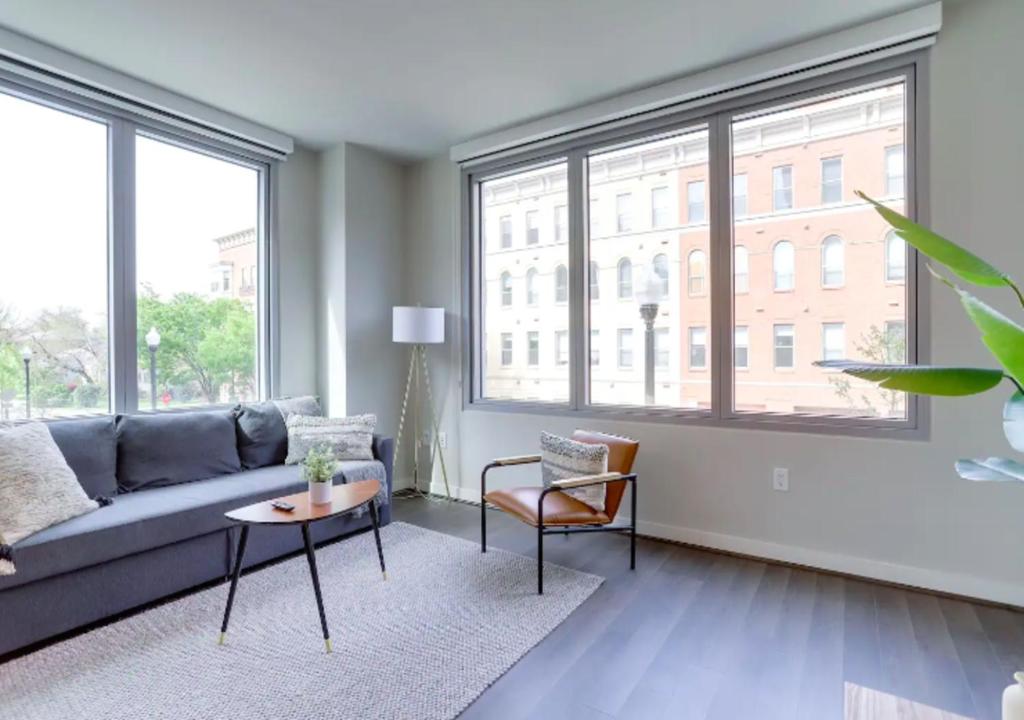 a living room with a couch and a table and windows at Wonderful 2BR Apartment At Clarendon With Gym in Arlington