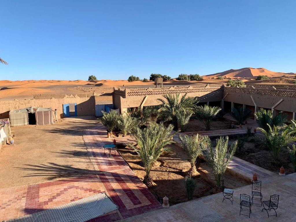 a house in the middle of a desert with palm trees at Maison Adrar Merzouga in Merzouga