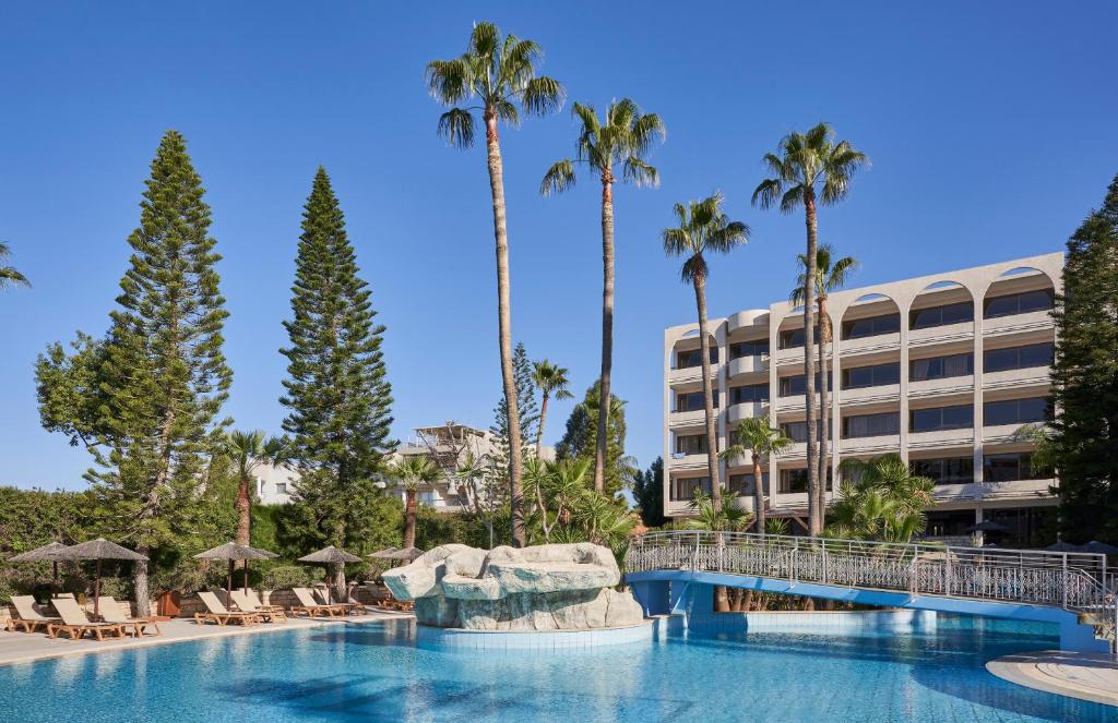 a swimming pool with palm trees and a building at Atlantica Oasis Hotel in Limassol