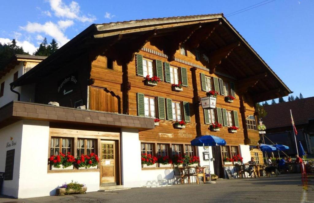 een groot houten gebouw met rode bloemen op de ramen bij Gasthaus Elsigbach in Achseten