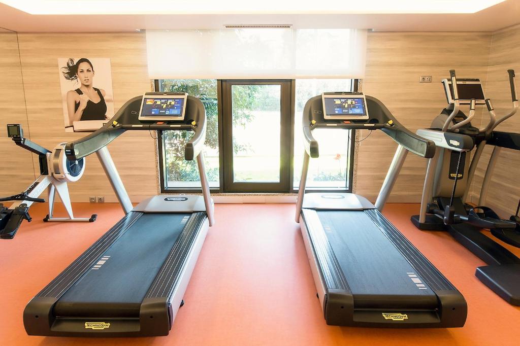 A bright cardio room has two treadmills, ellipticals and a rowing machine.