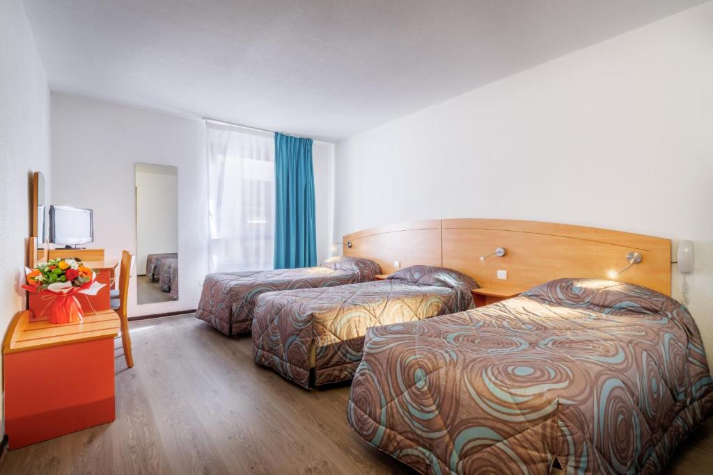 a hotel room with two beds and a table at Hôtel Ariane in Lourdes