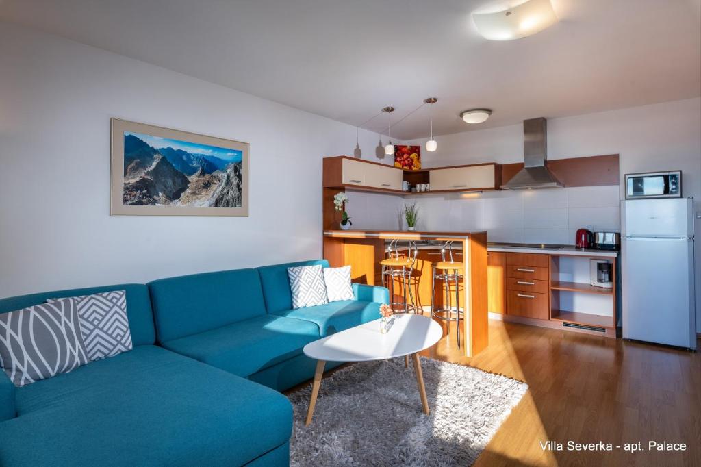 a living room with a blue couch and a kitchen at Apartmány Villa Severka in Vysoke Tatry - Novy Smokovec