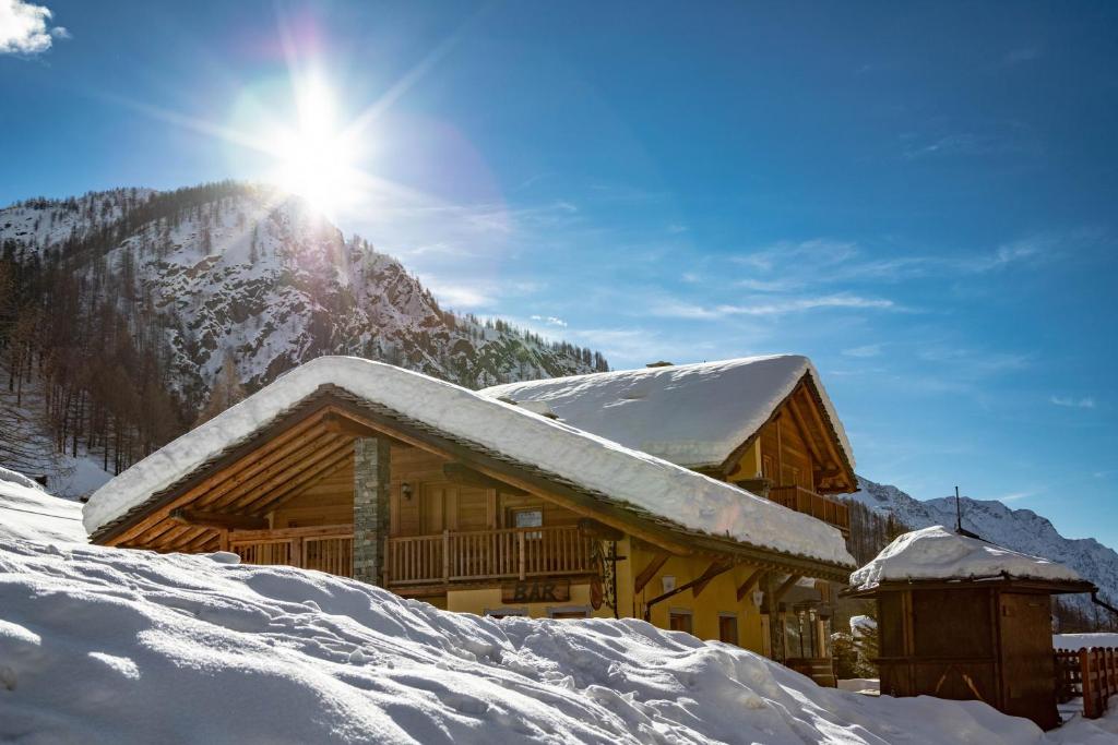 une cabane en rondins recouverte de neige avec le soleil derrière elle dans l'établissement Walsertal Residence, à Gressoney-La-Trinité