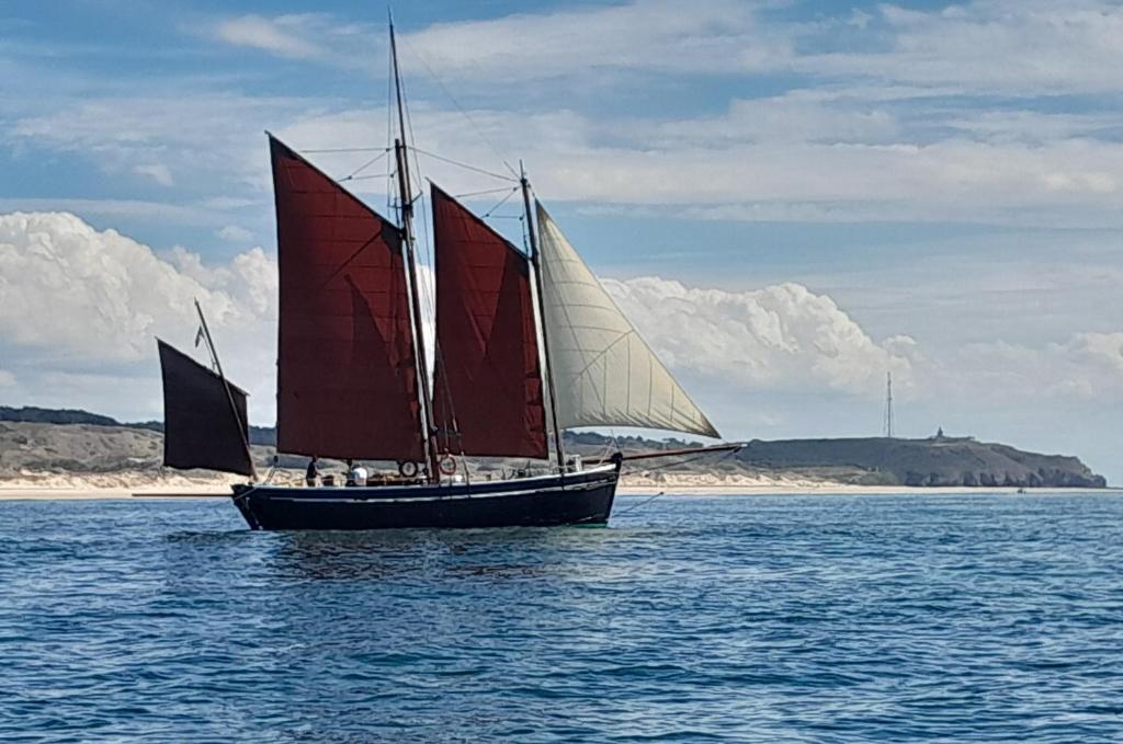 un velero con velas rojas en el agua en Proche port Centre village, en Barneville-Carteret