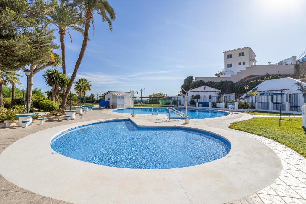 a swimming pool with palm trees and a building in the background at Casa La Intemporal in Nerja