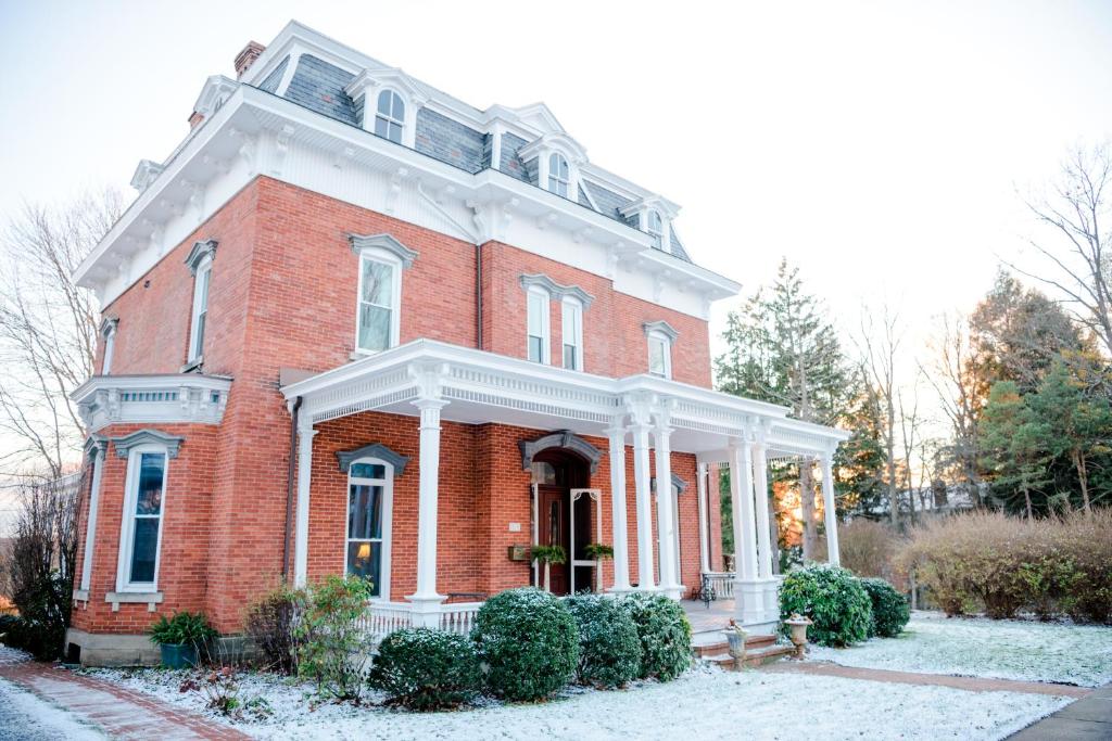 une maison en briques rouges avec une véranda blanche dans la neige dans l'établissement The Big Brickhouse, à Mercer