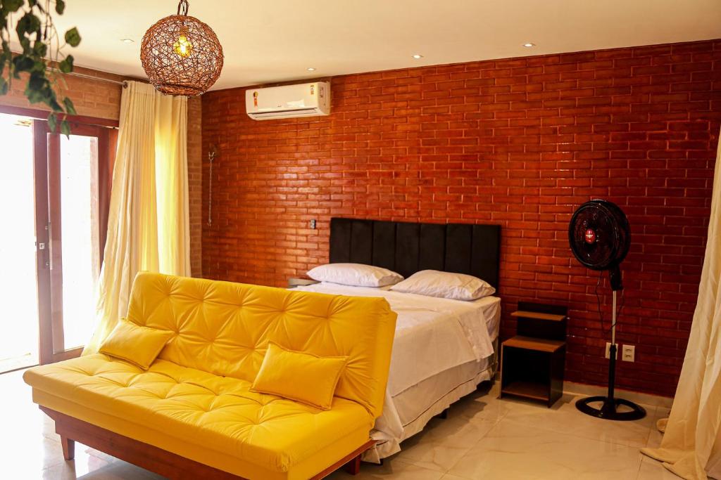 1 dormitorio con sofá amarillo y pared de ladrillo en Chale c churrasqueira a 5 min da Praia de Pipa RN, en Pipa