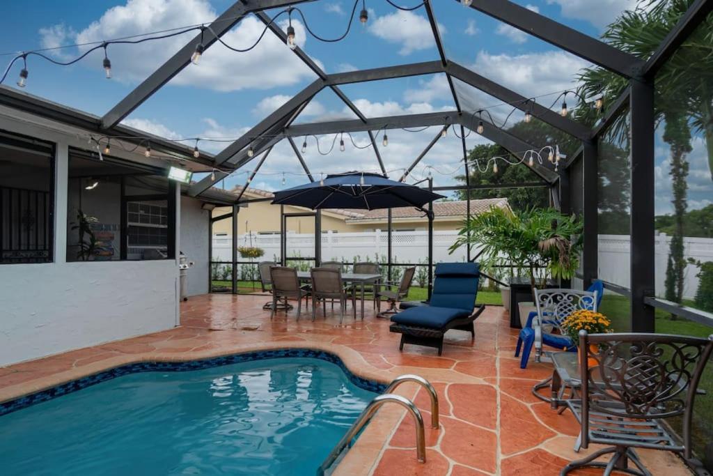 eine Terrasse mit einem Pool, Stühlen und einem Sonnenschirm in der Unterkunft Three Bedroom Pool Home with Modern Interior Design in Coral Springs