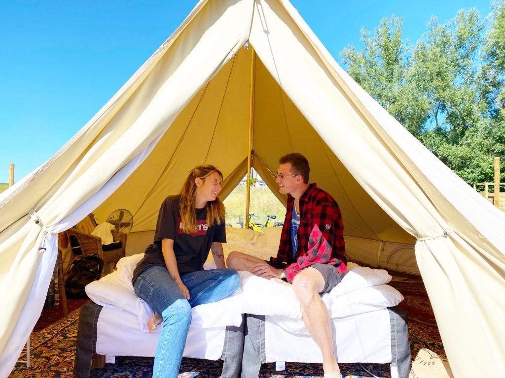 a man and woman sitting on beds in a tent at Gårdshotellets Camping in Ystad