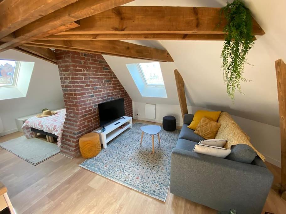 a living room with a couch and a brick wall at Chez Mathilde Studio Calais Nord Citadelle in Calais