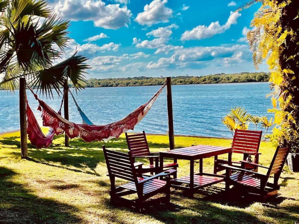 two chairs and a table with a hammock next to the water at Casa do Mangue-Paraíso na beira do rio Wi-Fi 300 M in Jaguaripe